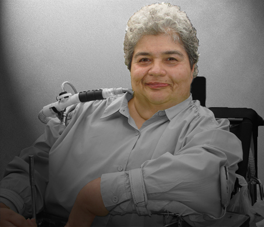 close-up of woman with short curly grey hair and a twinkle in her eyes. in powerchair with ventilator hose showing