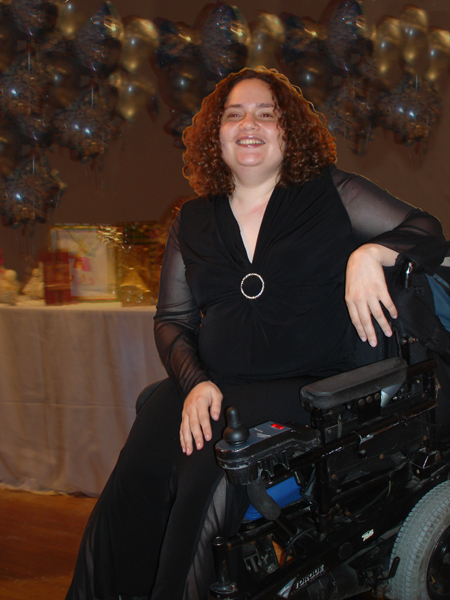 young woman in pretty black dress and big smile, sitting in her powerchair 